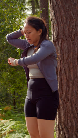 Vertical-Video-Of-Woman-Exercising-Doing-Work-Out-Outdoors-Running-Along-Track-In-Forest-Stopping-For-Breath-And-Checking-Activity-App-On-Smart-Watch-Shot-In-Real-Time-1